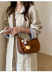 Detail of retro brown suede shoulder bag with cute teddy bear charm and sleek leather piping