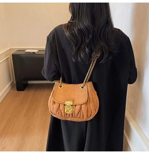 Detail view of brown suede handbag featuring pleat craftsmanship and gold buckle lock