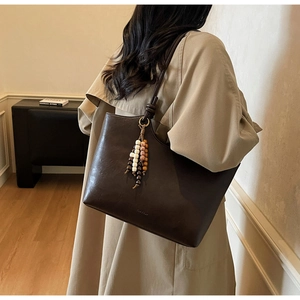 Detail of dark brown leather tote bag with ethnic wooden bead tassel on a beige coat