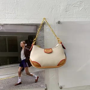 Détail du sac sous l'aisselle blanc cassé avec coins marrons et chaîne dorée élégante