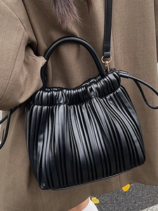 Minimalist black pleated bucket bag with drawstring closure and golden hardware