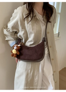 Minimalist dark brown crescent bag with plush bear charm detail on soft suede texture