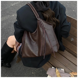 Gros plan d'un sac cabas marron foncé avec anses tressées et détails de longues franges