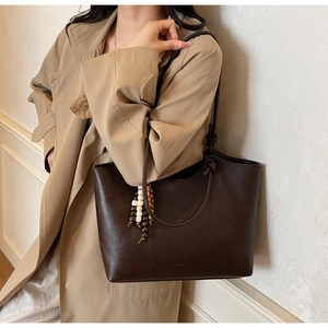 Detail of dark brown tote bag with beaded charm accessory on the handle and leather texture