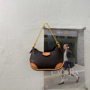 Détail du sac sous l'aisselle en cuir grainé avec bordure orange et bandoulière chaîne dorée