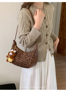 Detail of leopard print crescent bag with brown leather trim and a cute teddy bear charm