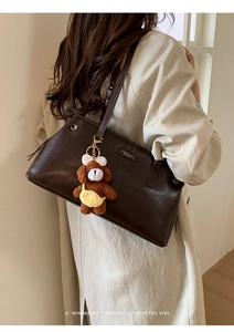 Detail of dark brown leather tote bag featuring a cute plush bear charm and metallic logo