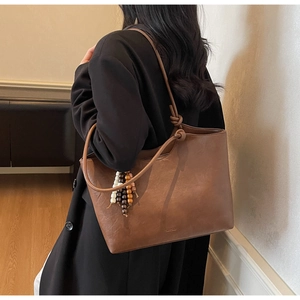 Brown leather tote bag featuring a beaded tassel charm and knotted shoulder strap detail