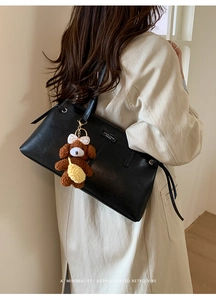 Close-up of black leather shoulder bag with a cute brown plush puppy bag charm