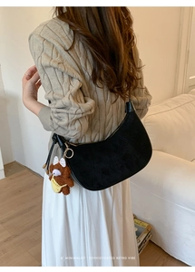 Detail of a black suede hobo bag with gold zipper and a cute brown bear charm