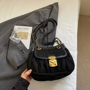 Detail view of black pleated handbag with vintage gold metal clasp on white bedding