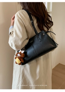 Detail of minimalist black PU leather shoulder bag with plush bear charm on beige coat