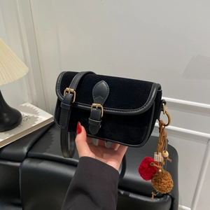 Close-up of black velvet crossbody bag with leather trim and colorful pompom charms
