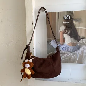Detail view of coffee brown suede crescent bag with a decorative plush bear keychain