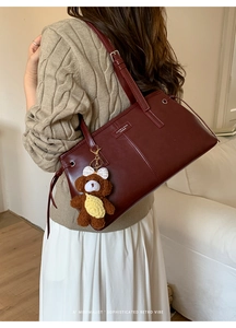 Detail of burgundy leather tote bag with brand lettering and brown plush bear charm accessory