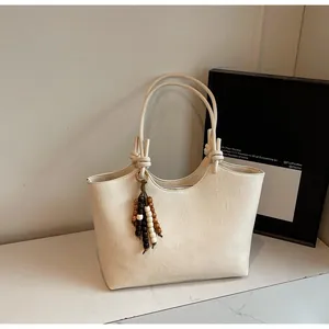 Detail of cream white faux leather tote bag featuring a beaded tassel and knot handle decor