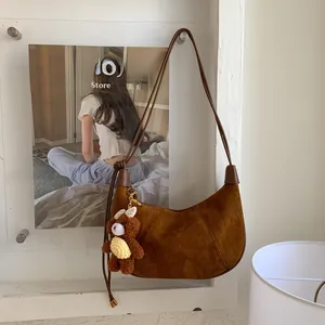 Detail of suede hobo bag featuring leather piping and a brown plush bear charm