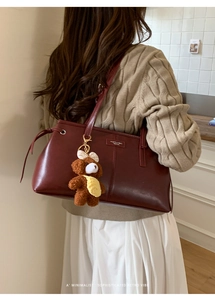 Detail of dark red vintage underarm bag with metal tag and cute plush bear charm