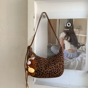 Detail of leopard print crescent bag with brown strap and cute teddy bear charm