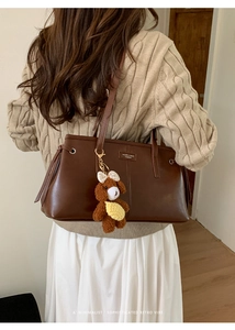 Detail of dark brown leather tote bag with brand logo patch and cute teddy bear charm