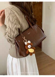 Detail view of deep brown leather tote bag with metallic logo and plush bear charm