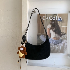 Minimalist black hobo shoulder bag with a plush bear charm hanging on a white wall