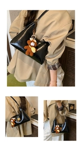 Detail of glossy black hobo bag with cute plush bear pendant and thin shoulder strap