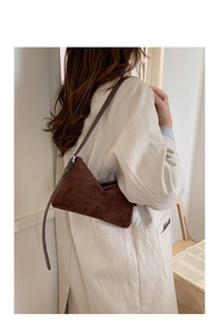 Détail du sac à bandoulière marron mat vintage porté avec un trench-coat beige
