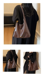 Detail of deep brown glossy Hobo bag featuring a gold logo and fuzzy ball charm pendant