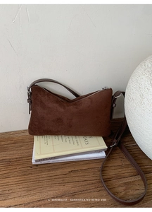 Détail d'un sac en daim marron avec fermeture éclair argentée et bandoulière en cuir