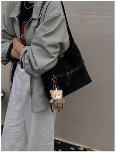 Detalle de bolso hobo negro con textura de leopardo, colgante de oso y hebilla metal