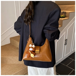 Close-up of a brown leather shoulder bag featuring a cute plush bear charm and metallic zipper