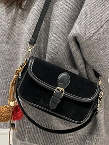 Minimalist black suede crossbody bag with gold hardware and plush charms on a model