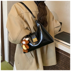 Close-up of black patent leather shoulder bag with gold buckle and plush bear charm