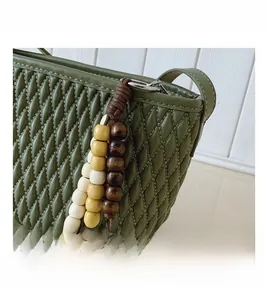 Detail of dark green quilted handbag featuring a three-color beaded wooden charm