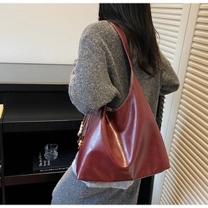 Detail view of burgundy leather tote bag featuring a wooden bead tassel and side brand logo