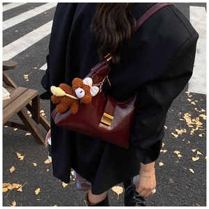 Detail view of burgundy leather shoulder bag with gold clasp and cute plush bear charm