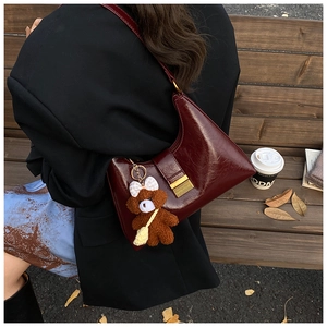 Deep red hobo bag on a wooden bench with autumn leaves and cute bear pendant