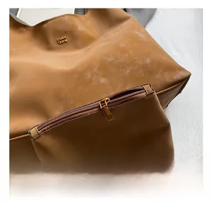 Gros plan du sac en cuir brun avec logo doré et petite pochette zippée assortie