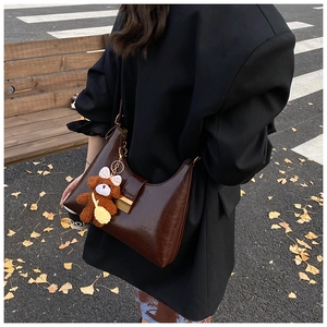 Detail of dark brown glossy underarm bag with a cute plush bear charm in street style