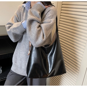 Detail of minimalist black leather tote bag featuring a gold logo and high-quality stitching