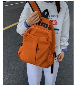 Close-up of bright orange nylon sports backpack featuring bold black letter printing and cords
