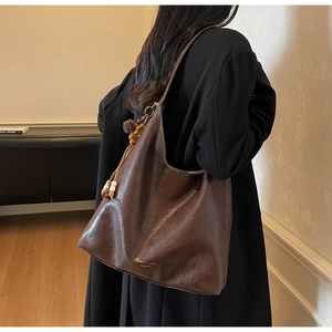 Detail of dark brown leather tote bag with vintage tassel charm and gold brand logo