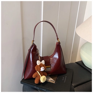 Close-up of a burgundy shoulder bag with glossy finish and cute brown bear pendant detail