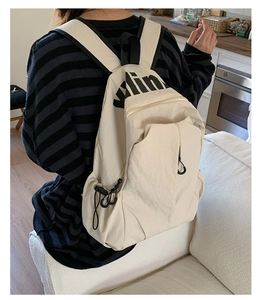 Detail of cream nylon backpack featuring black letter prints and functional side drawstrings