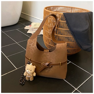 Detalle del bolso de ante marrón con asa trenzada y colgante de osito de peluche
