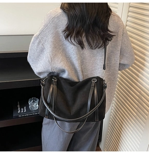 Detail of a large black tote bag in suede texture with adjustable shoulder straps and top handles