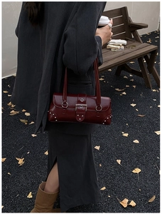 Dark red tote bag with silver rivets shown on model shoulder in autumn outdoor setting