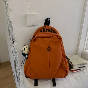 Detail of orange nylon backpack with black lima logo and cute white puppy plush charm