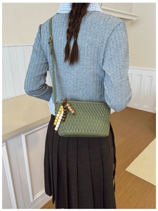 Detailed view of dark green pleated bucket bag with tassel and rhombus pattern